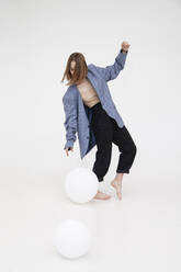 Young woman playing with white balloon against white background - IYNF00112