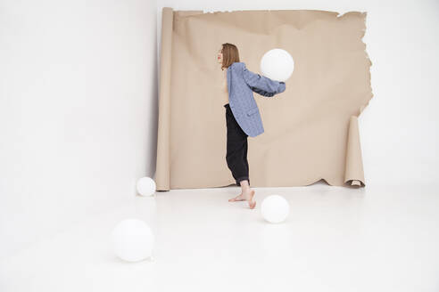 Junge Frau balanciert Luftballon auf Händen vor braunem Hintergrund - IYNF00115