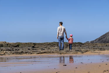 Father and daughter standing on rock at beach - DIGF17779