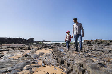 Happy father and daughter standing on rock at beach - DIGF17780