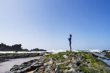 Frau mit verschränkten Händen auf einem Felsen am sonnigen Strand stehend - DIGF17784