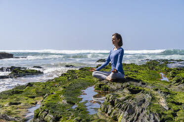 Frau sitzt im Lotussitz und meditiert auf einem Felsen am Strand - DIGF17785