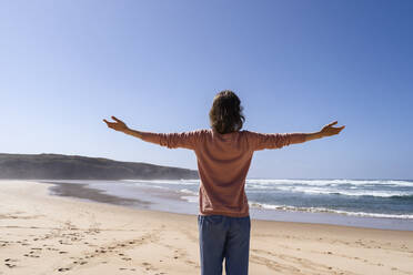 Woman with arms outstretched standing at beach on sunny day - DIGF17789