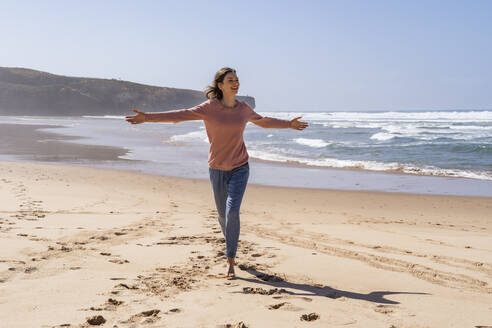 Happy woman with arms outstretched running at beach on sunny day - DIGF17790