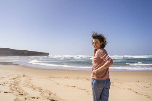 Glückliche Frau, die an einem sonnigen Tag am Strand dem Meer entgegenläuft - DIGF17794