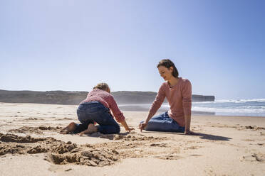 Mother and daughter writing on sand at beach - DIGF17795