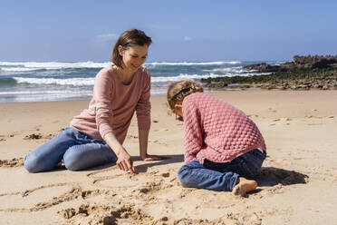 Glückliche Mutter und Tochter schreiben auf Sand am Strand - DIGF17796