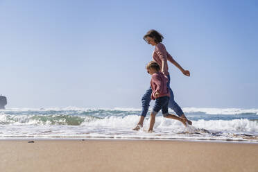 Glückliche Mutter und Tochter laufen im Wasser am Strand an einem sonnigen Tag - DIGF17800