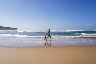 Vater und Tochter laufen am Strand an einem sonnigen Tag - DIGF17802