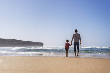 Father and daughter walking towards sea on sunny day - DIGF17803