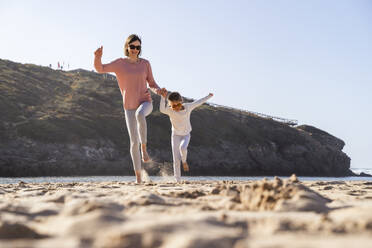 Glückliche Mutter und Tochter springen am Strand in den Sand - DIGF17807
