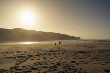 Vater mit Tochter spazieren am Strand bei Sonnenuntergang - DIGF17809