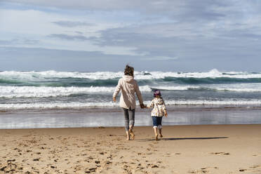 Mutter und Tochter gehen am Strand auf die Wellen zu, die an einem sonnigen Tag plätschern - DIGF17820