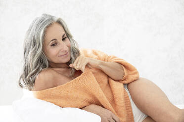 Lächelnde Frau mit grauem Haar, die zu Hause auf dem Bett liegt - JBYF00142