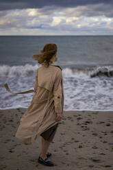 Frau im Mantel stehend mit Blick auf das Meer - SSGF00558