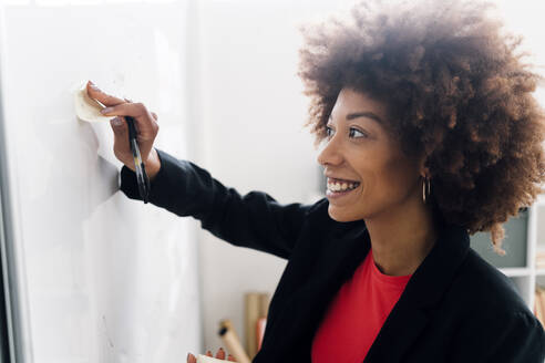 Geschäftsfrau klebt Notiz auf Whiteboard im Büro - GIOF15137