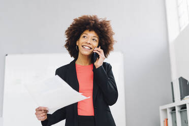 Lächelnde Geschäftsfrau, die im Büro mit einem Mobiltelefon spricht - GIOF15164