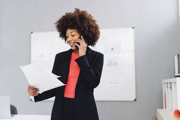 Businesswoman examining document and talking on mobile phone in office - GIOF15165