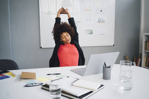 Tired young businesswoman stretching at desk in office - GIOF15171