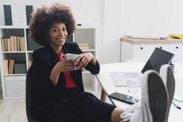 Smiling young businesswoman sitting at desk with coffee cup in office - GIOF15179