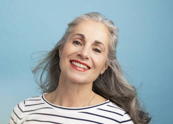 Glückliche Frau mit grauem Haar vor blauem Hintergrund - JBYF00148