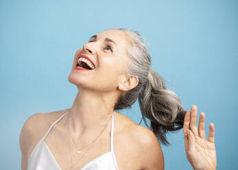 Happy woman with gray hair standing against blue background - JBYF00154