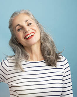 Glückliche Frau mit grauem Haar trägt gestreiftes weißes T-Shirt vor blauem Hintergrund - JBYF00164