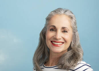 Lächelnde Frau mit grauem Haar auf blauem Hintergrund - JBYF00165