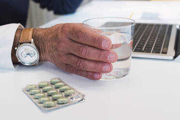 Hand of freelancer holding glass of water by pills - PNAF03542