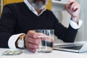 Freiberufler mit einem Glas Wasser am Tisch sitzend - PNAF03544