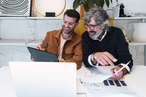 Happy young freelancer sharing tablet PC with colleague sitting at table - PNAF03592