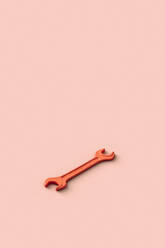 Three dimensional render of orange colored wrench lying against beige background - GCAF00181