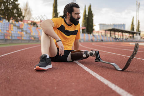 Sportler mit Beinprothese auf der Laufbahn sitzend - JCCMF06002