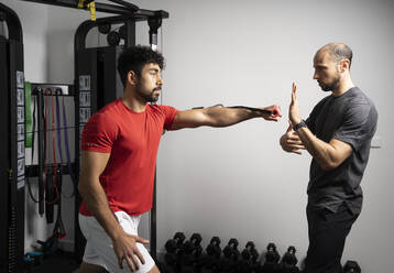 Fitnesstrainerin, die einem jungen Sportler im Fitnessstudio bei seinen Übungen hilft - DAMF00917