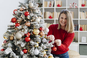 Glückliche Frau beim Schmücken des Weihnachtsbaums zu Hause - GIOF15208