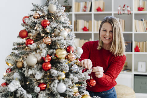 Glückliche Frau beim Schmücken des Weihnachtsbaums zu Hause - GIOF15208