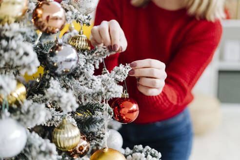 Frau schmückt Weihnachtsbaum mit Christbaumkugel zu Hause - GIOF15209