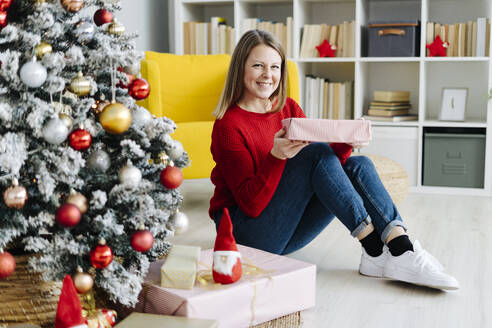 Glückliche Frau mit Geschenk unter dem Weihnachtsbaum zu Hause - GIOF15211