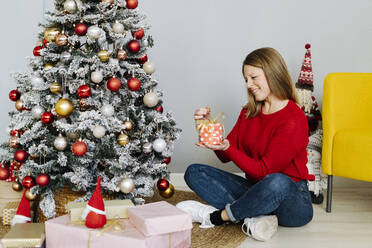 Glückliche Frau, die zu Hause sitzend Weihnachtsgeschenke öffnet - GIOF15212