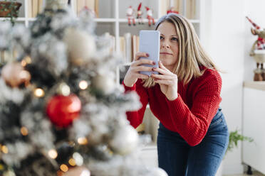 Woman photographing Christmas tree through mobile phone at home - GIOF15222