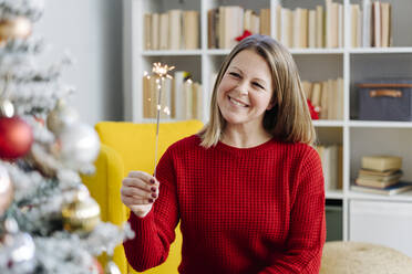 Glückliche Frau mit Wunderkerze vor einem Weihnachtsbaum zu Hause - GIOF15227