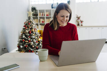 Lächelnde Frau mit Laptop und Kaffeetasse am Tisch sitzend - GIOF15229