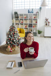 Glückliche Frau mit Kaffeetasse am Wohnzimmertisch sitzend - GIOF15235