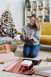 Lächelnde Frau verpackt Geschenke mit Geschenkpapier zu Hause - GIOF15249