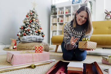 Glückliche Frau verpackt Geschenke mit Geschenkpapier zu Hause - GIOF15250