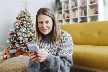 Lächelnde Frau mit Mobiltelefon im Wohnzimmer zu Hause - GIOF15254