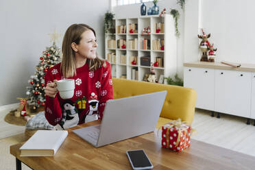 Blonde Frau mit Laptop und Kaffeetasse sitzt am Tisch - GIOF15276