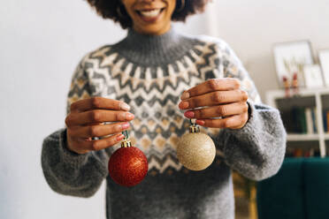 Lächelnde Frau hält zu Hause Weihnachtskugeln in der Hand - GIOF15279