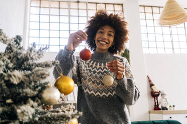 Glückliche Frau hält zu Hause eine Weihnachtskugel in der Hand - GIOF15280