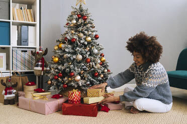 Smiling woman arranging gifts by Christmas tree at home - GIOF15289